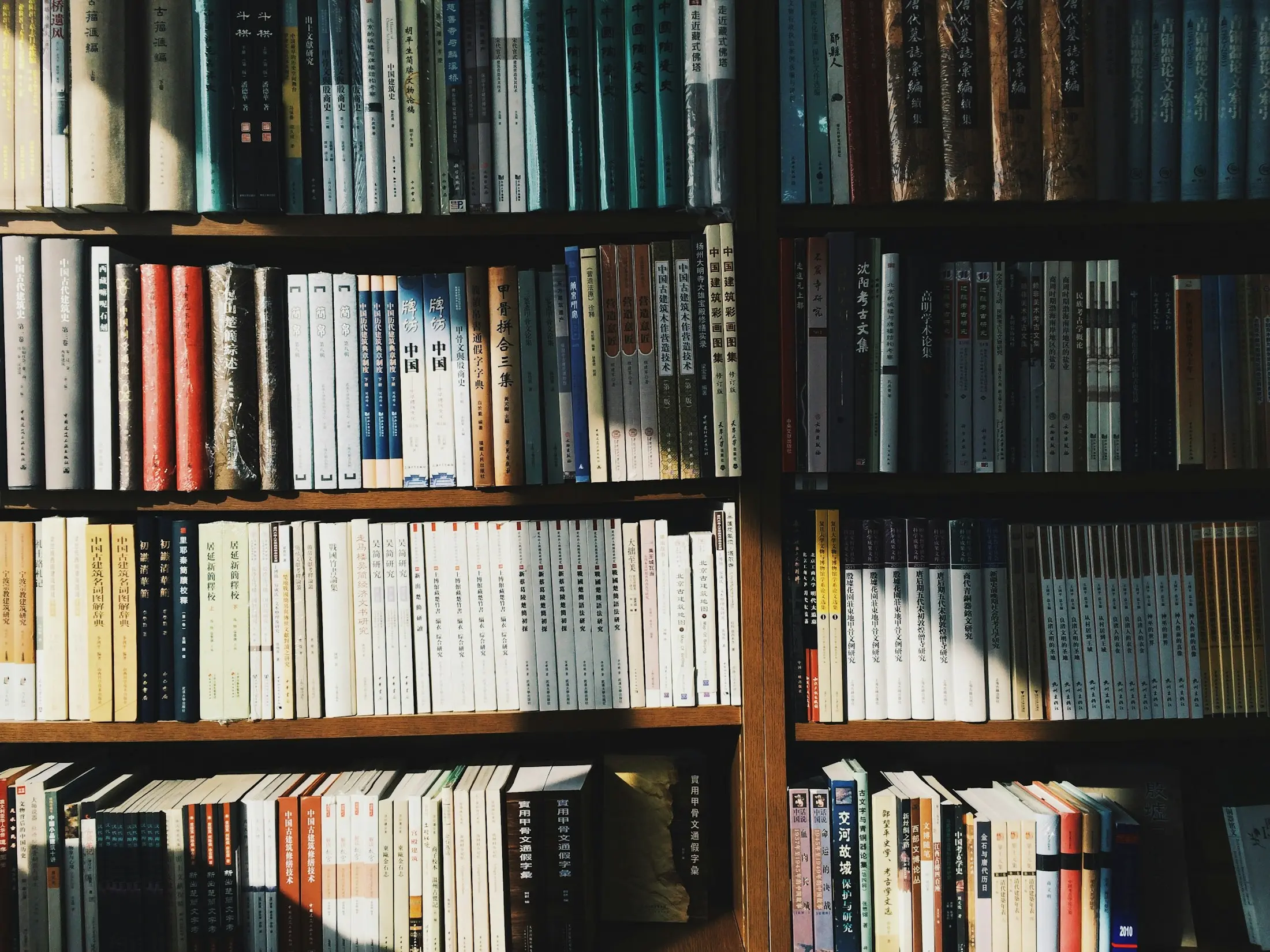 Солнечный свет проходит по корешкам книг на тёмной полке